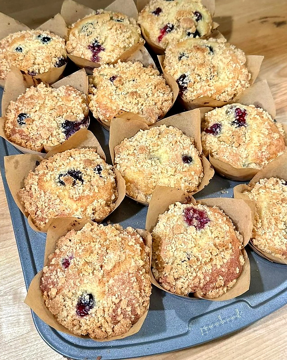A tin of freshly baked berry muffins with crumb topping